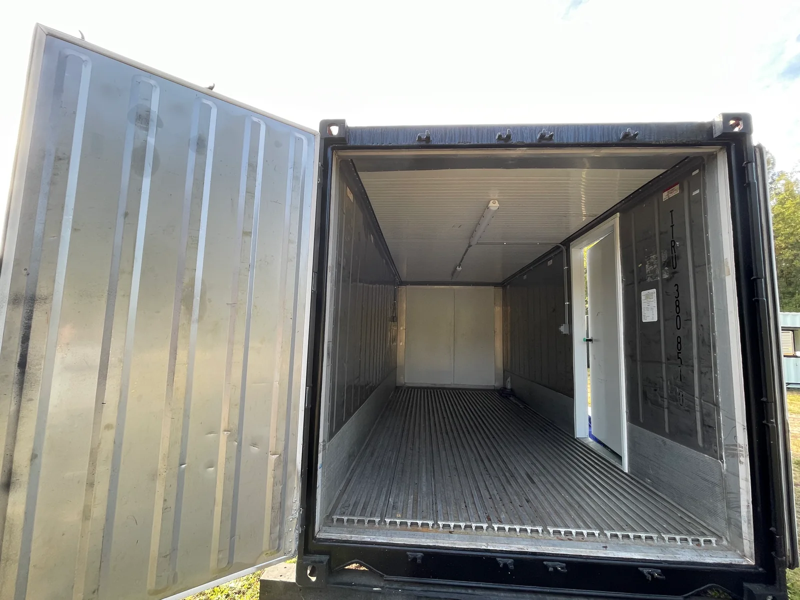 Open insulated shipping container with a personnel door in its interior side wall.